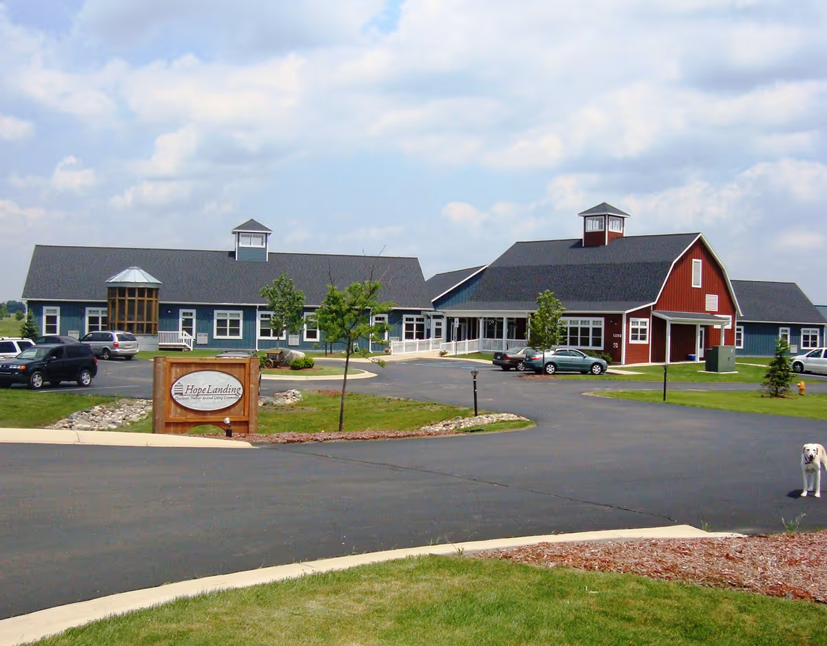 Front view of the Hope Landing senior living facility showing a barn-style building, parking lot, and wooden entrance sign.