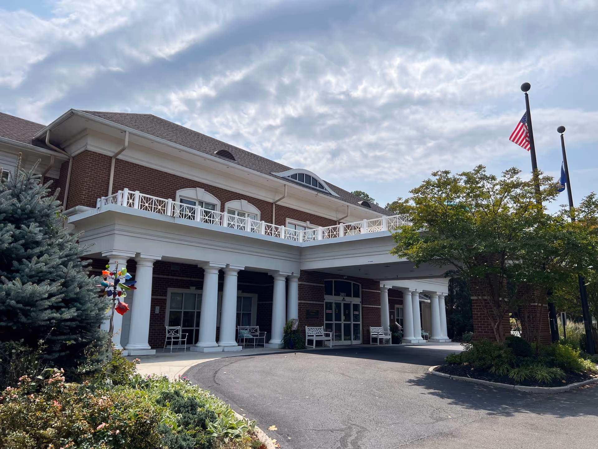 Brick senior living facility with white columns, entrance, and flagpoles.