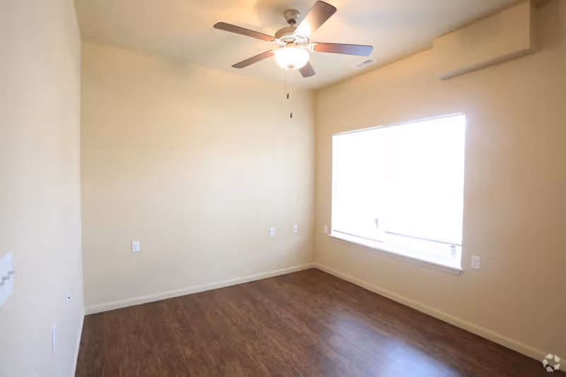 Empty room with beige walls, a ceiling fan with light, a large window with blinds, and wood flooring.