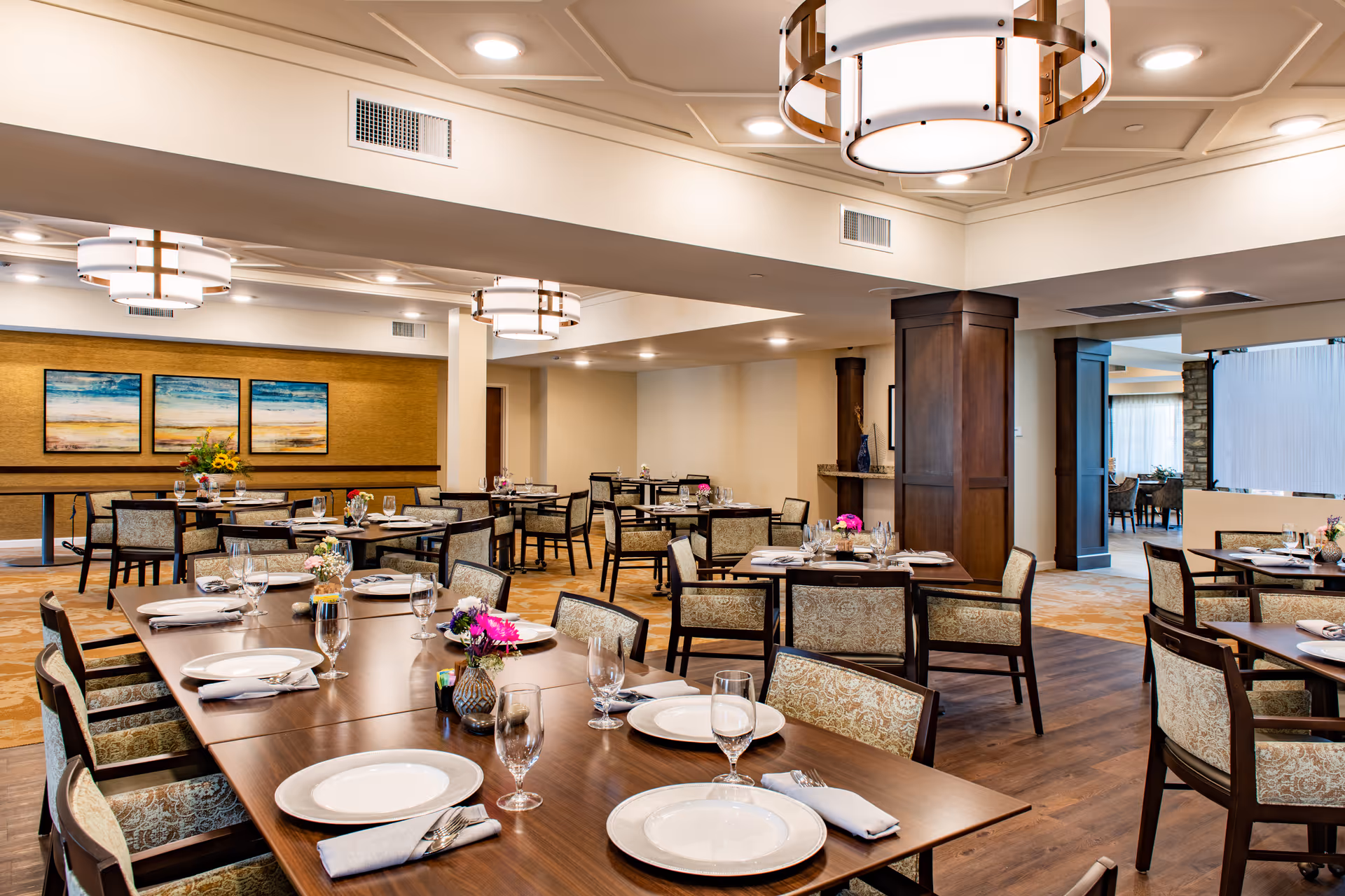 Bright, upscale dining room with multiple set tables and chairs, modern light fixtures, and wall artwork.