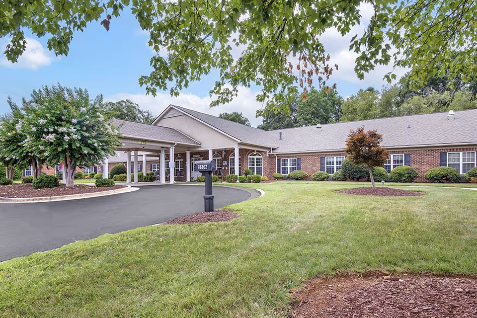 Front exterior of a single-story brick senior living building with a covered entrance, circular driveway, mailbox, and landscaped lawn.