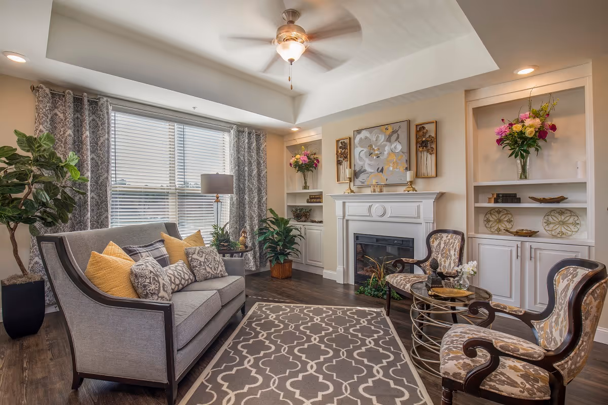 Bright, well-decorated living room with a sofa, patterned chairs, fireplace with built-in shelves, and a large window with curtains.