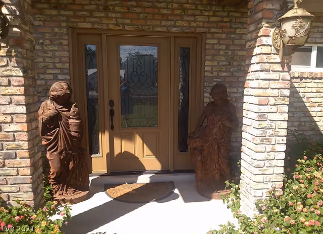 Brick front entrance with a tan double door flanked by two carved statues and a doormat.