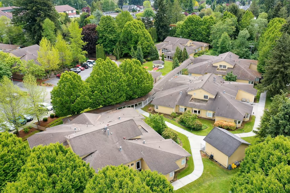 Aerial view of a senior living campus with multiple connected single-story cottages, paved walkways, and surrounding trees.