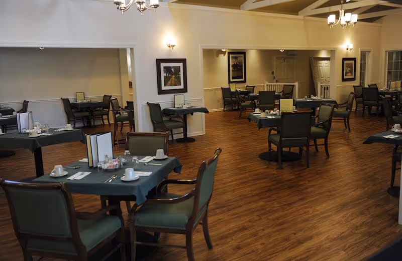 Spacious dining room with multiple set tables and green upholstered chairs on wood flooring.
