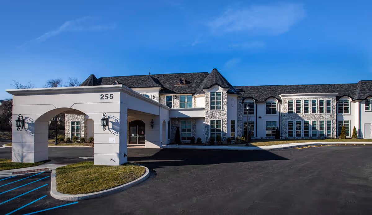 Front exterior view of The Remington of Yardley building with a covered entrance marked with the number 255, surrounded by a paved driveway and some grass areas under a clear blue sky.
