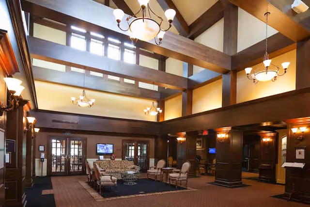 Spacious two-story lobby with exposed wooden beams, chandeliers, and a central seating area with sofas and chairs.