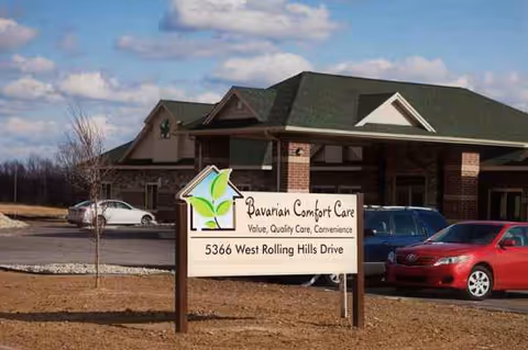 Exterior view of Bavarian Comfort Care building with sign and parked cars in front.