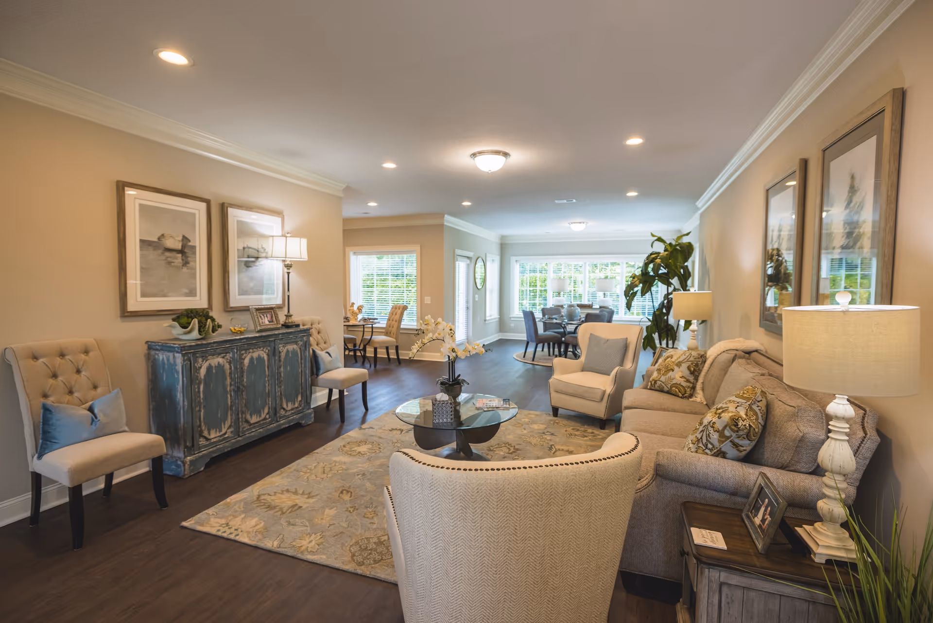 Well-lit open living room with sofas, armchairs, a coffee table, and a dining area in the background.
