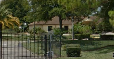 Gated entrance and landscaped grounds in front of a low-rise retirement center building with trees and shrubs.