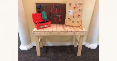 Wooden workbench with pegboard, red toolbox, and assorted hand tools in an interior workshop.