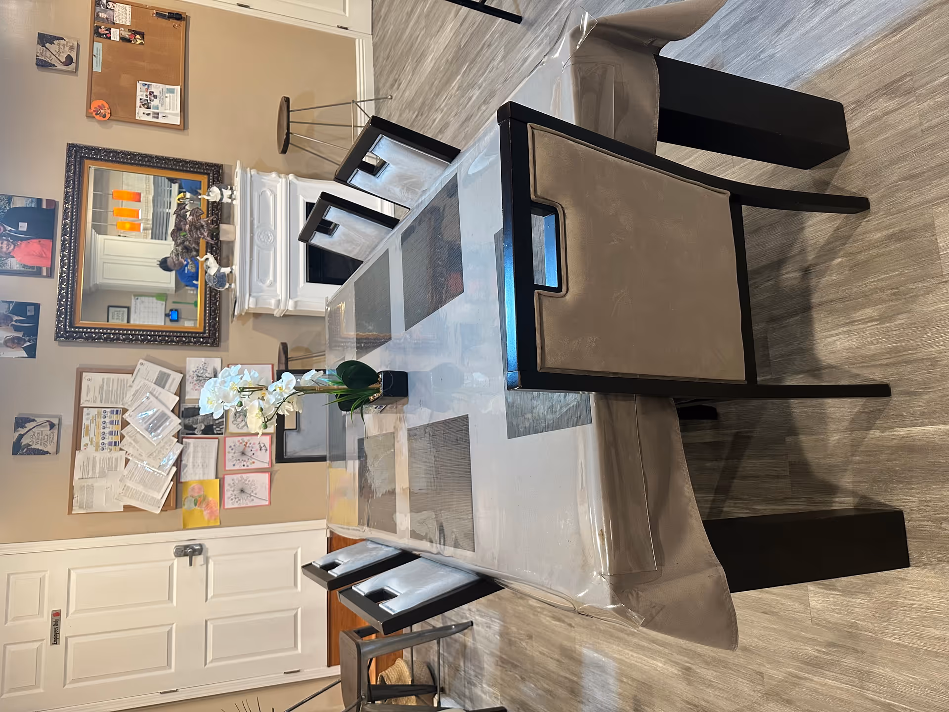 A dining room in a senior residence with a glass table, black chairs, and wall decor
