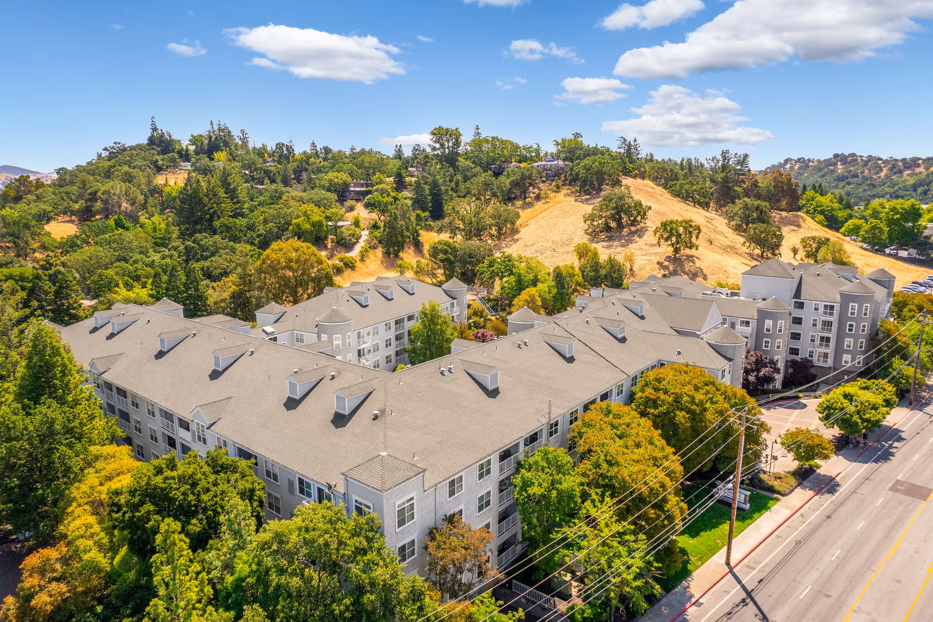 Aerial view of a multi-building senior living complex next to a road with trees and a hillside in the background.