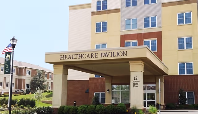 Entrance canopy of the multistory Healthcare Pavilion at Lutheran Community at Telford with landscaping and a flagpole.