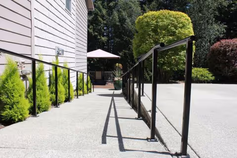 Outdoor ramp walkway beside a beige building leads to a patio with umbrella