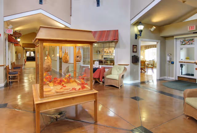 Entrance lobby of Milford Place showing a central glass display case with autumn decorations, wicker seating, and hallways to common areas.