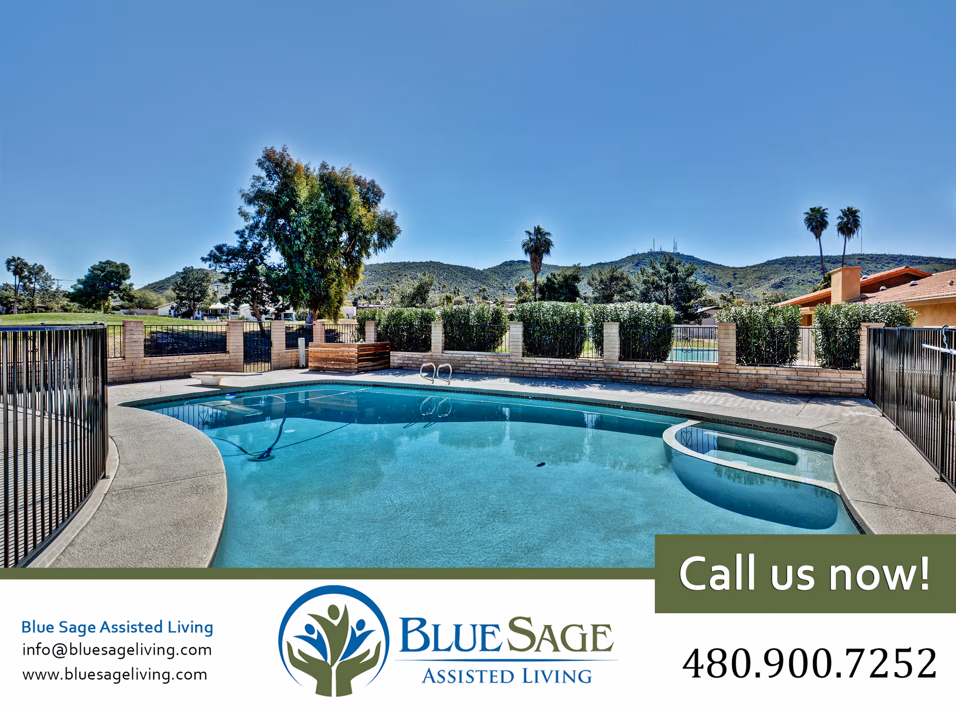 Outdoor swimming pool area at Blue Sage Assisted Living with clear blue water, surrounded by a safety fence and landscaping. In the background, there are trees, shrubs, and hills under a clear blue sky.