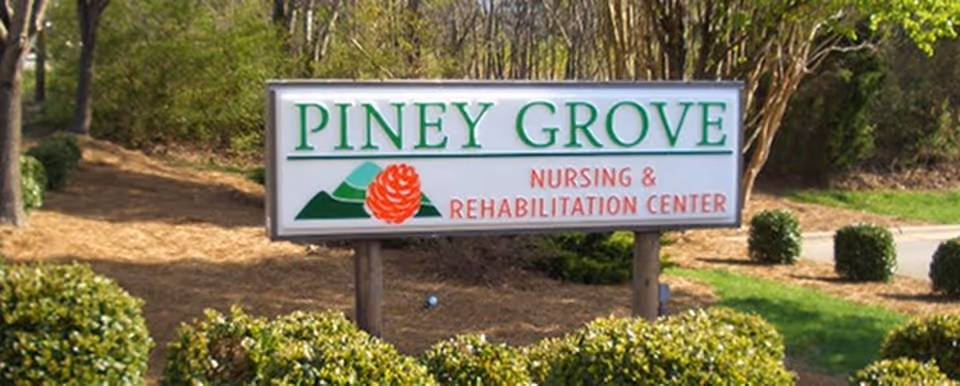 Outdoor view of a sign for Piney Grove Nursing & Rehabilitation Center surrounded by bushes and trees.