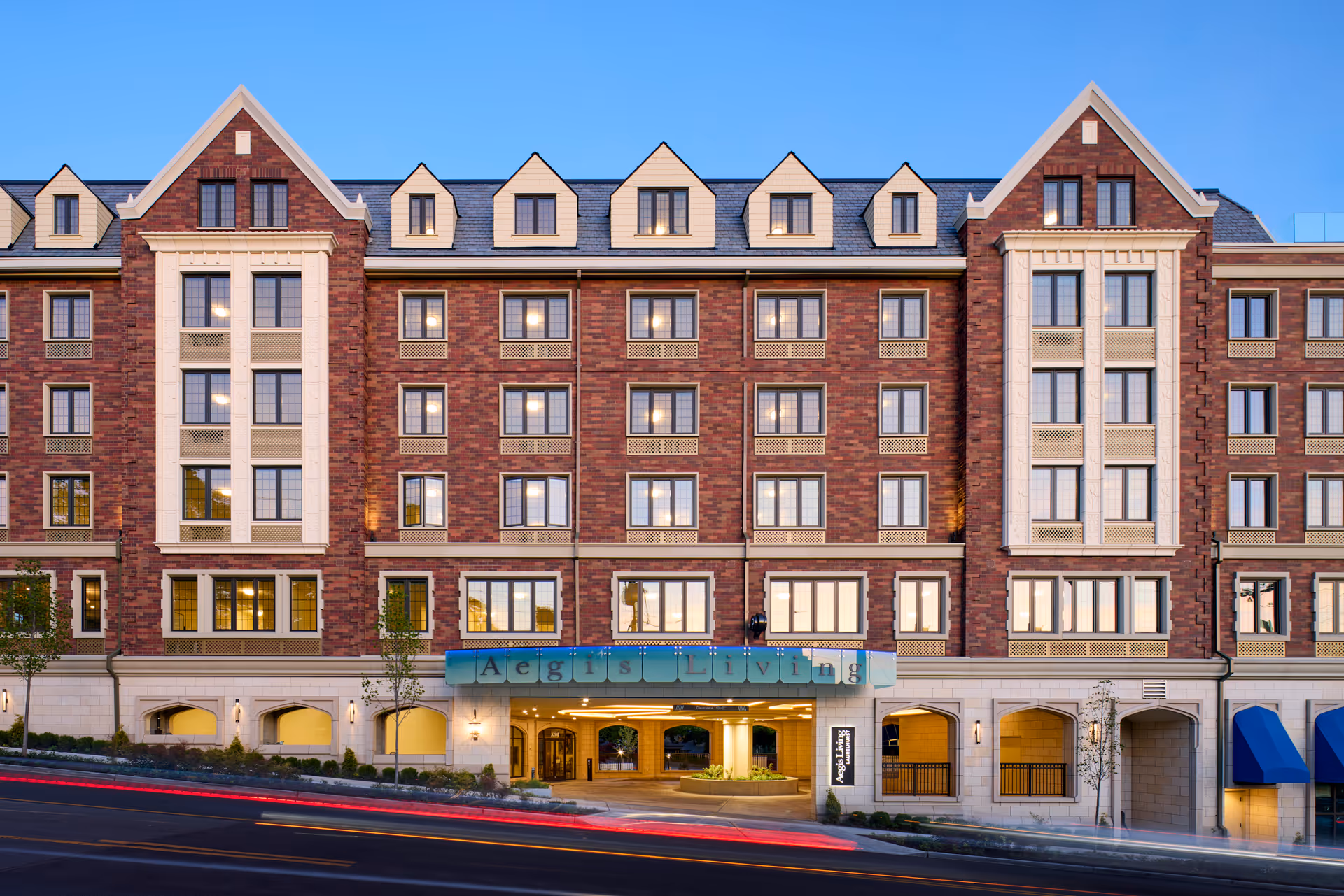 Exterior front view of a multi-story senior living facility named Aegis Living Laurelhurst, featuring a brick facade with multiple windows, a blue sign with the facility name above the entrance, and a clear blue sky in the background.