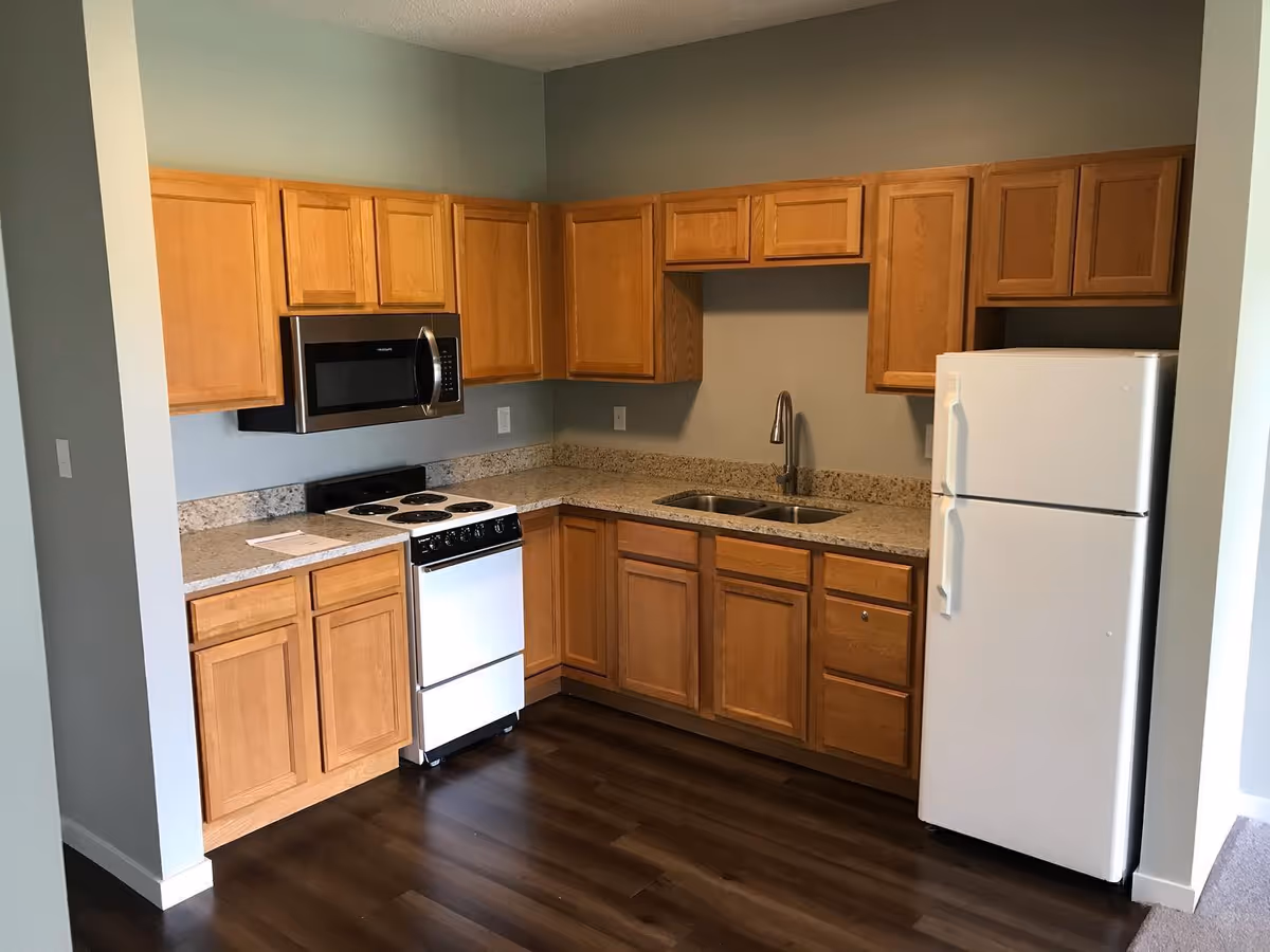 Compact kitchen with light wood cabinets, granite countertops, a white refrigerator and stove, microwave, and a double sink.