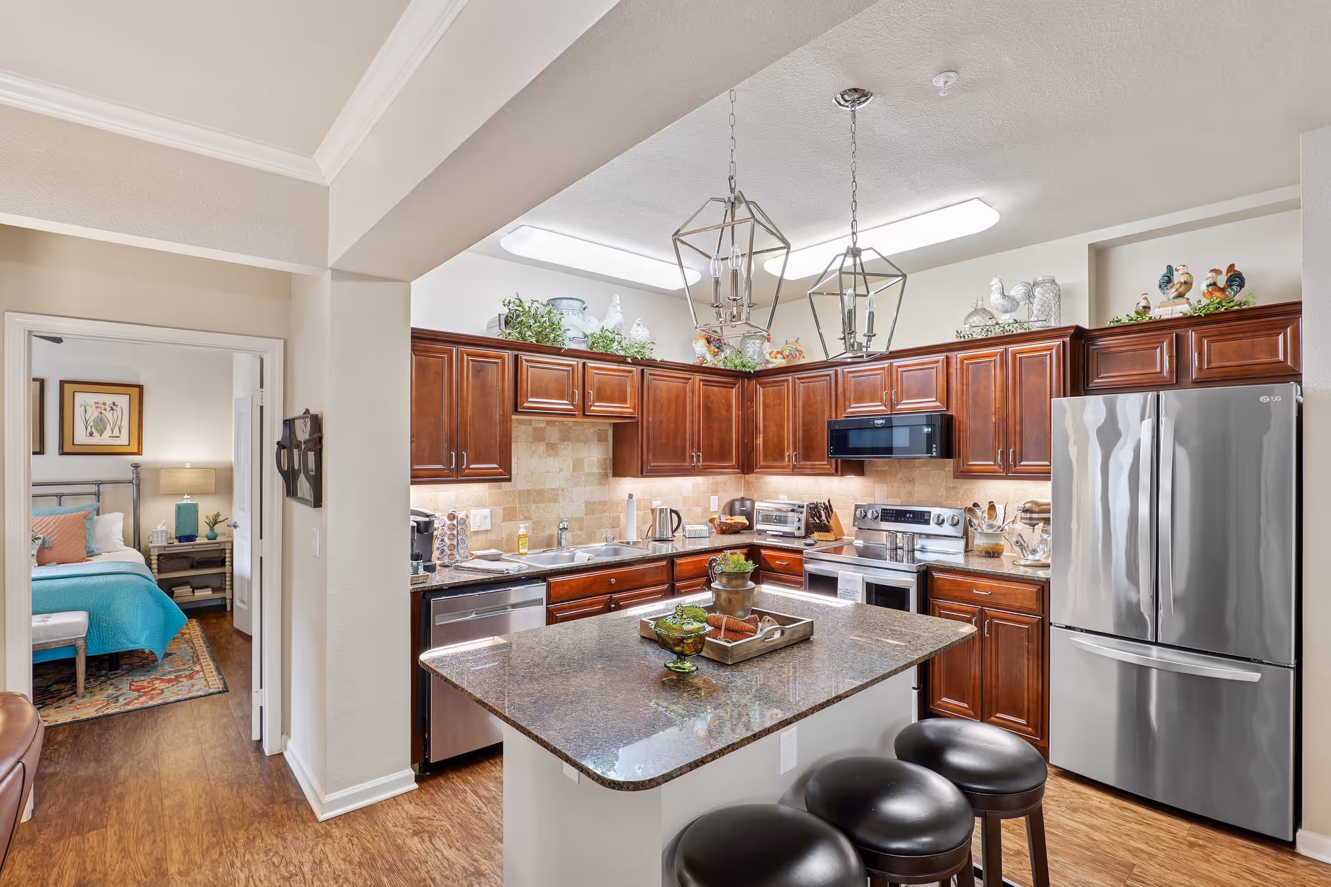 Bright modern kitchen with a central island, dark wood cabinets, stainless steel appliances, and a view into an adjacent bedroom.