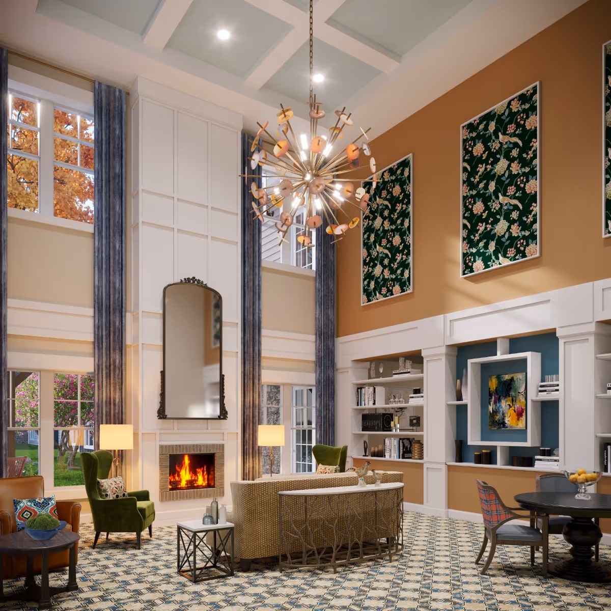 A spacious and elegant living room with high ceilings, large windows with blue curtains, a lit fireplace beneath a tall mirror, and comfortable seating including green armchairs and a beige sofa. The room features patterned carpet flooring, built-in white bookshelves with decorative items, a round black table with chairs, and three large floral artworks on a warm brown wall. A modern chandelier hangs from the ceiling.