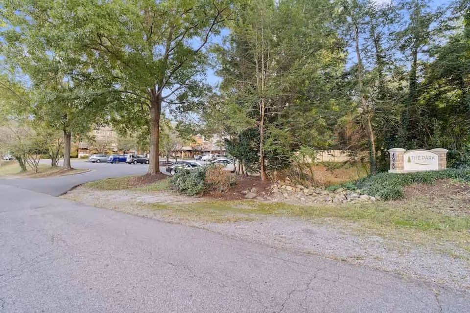 Exterior view of the facility entrance and parking area surrounded by trees with a stone sign reading 'The Park'.