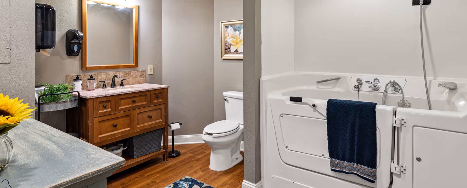 Bathroom featuring a walk-in bathtub with a navy towel, wooden vanity with mirror, toilet, and hardwood floor.