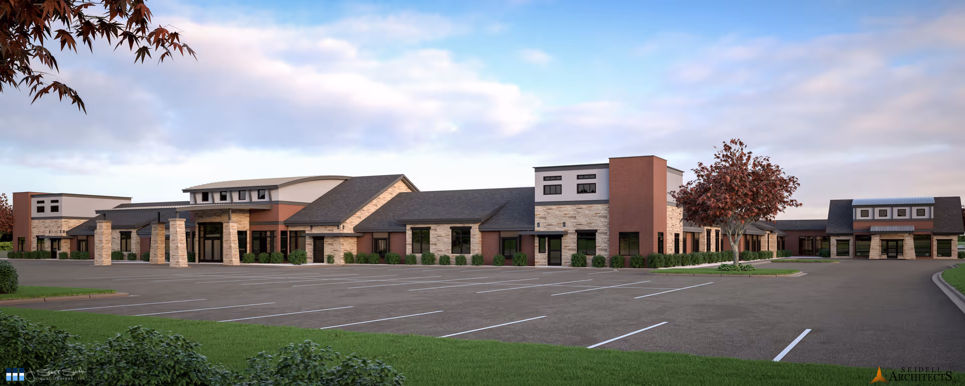 Exterior view of a single-story senior living facility building with a large empty parking lot in front, surrounded by green grass and a few trees with autumn-colored leaves under a partly cloudy sky.