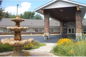 Exterior view of the Brittany Manor entrance showing a three-tiered stone fountain, covered porte-cochere, and surrounding landscaping.