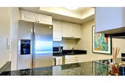 Modern kitchen with white cabinets, a stainless steel refrigerator, black granite countertops, a microwave, and a colorful framed artwork on the wall.
