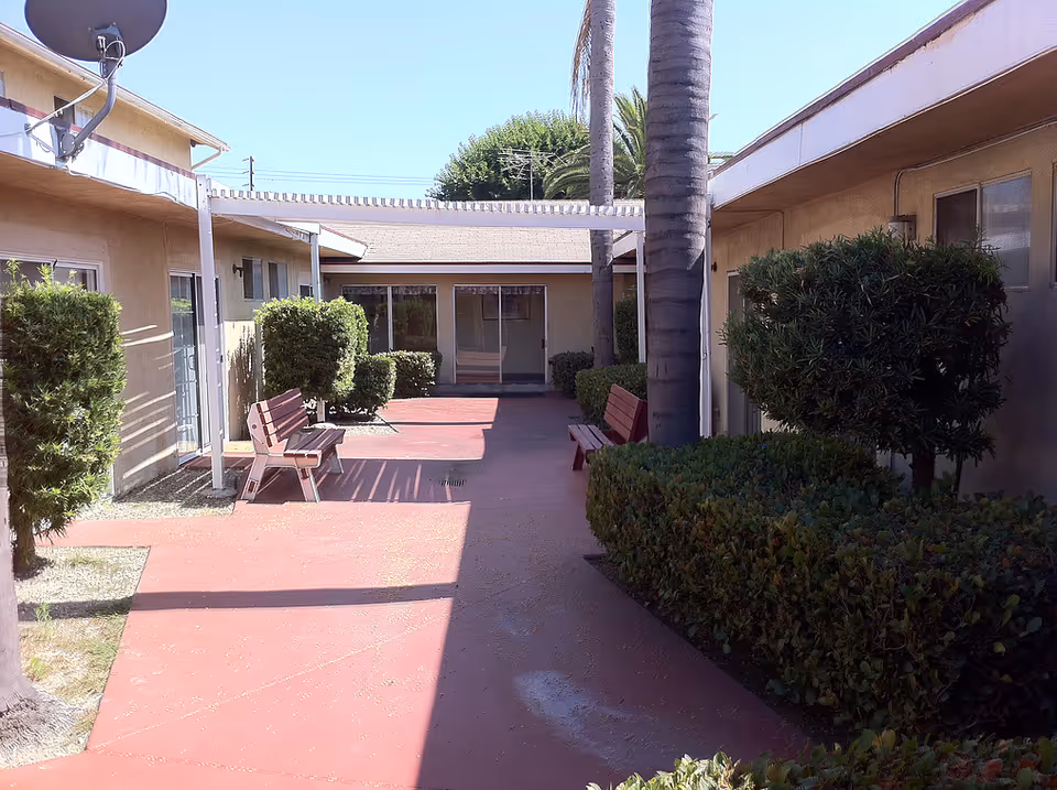 Outdoor courtyard of a senior living facility with benches, hedges, and concrete walkways.