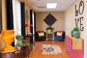 Bright sitting room with two armchairs, a colorful rug, decorative wall art including the word 'LOVE', and several potted plants.