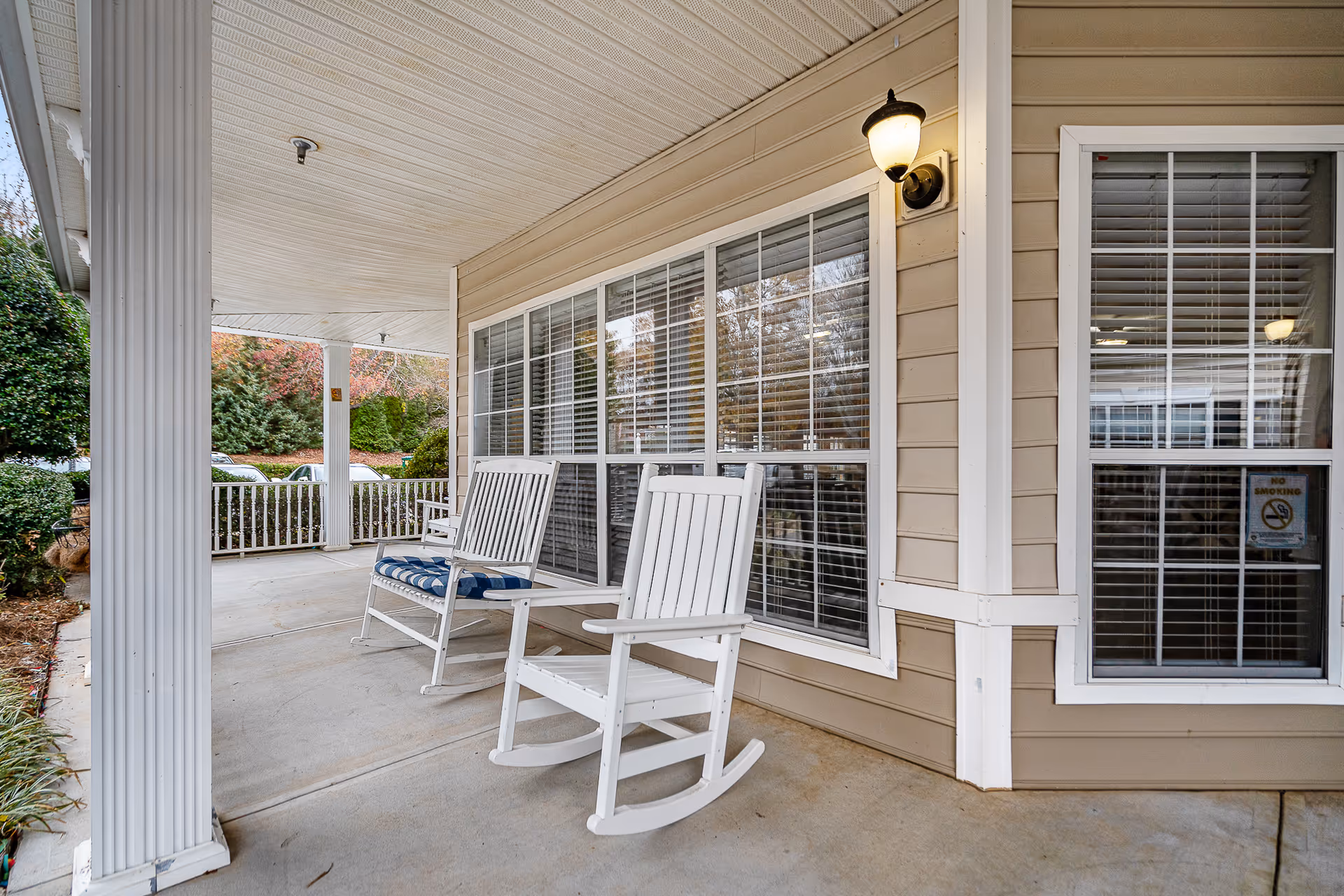 Covered front porch of a senior living facility with two white rocking chairs and large windows.