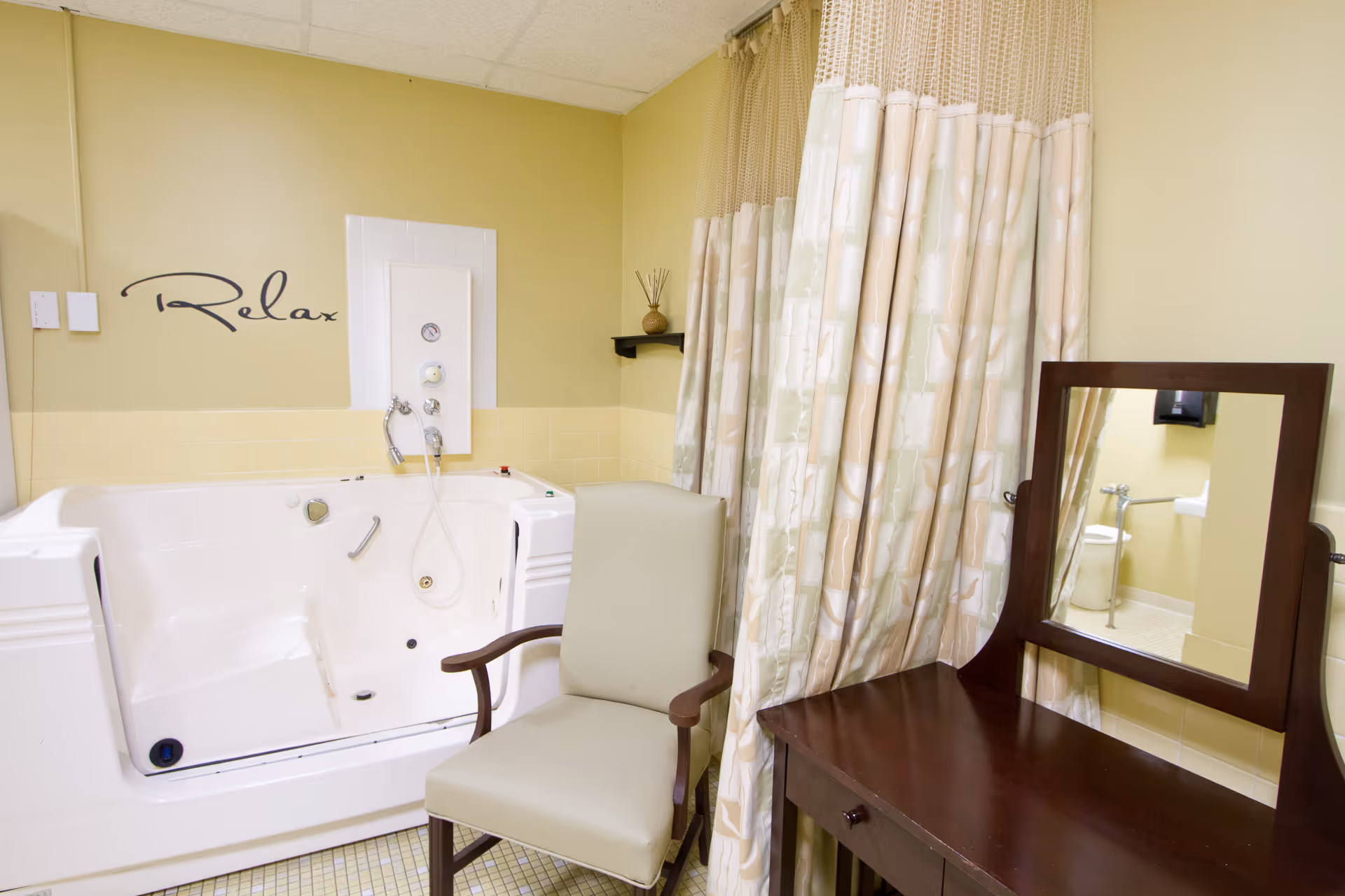 Walk-in bathtub with a chair, vanity and mirror in a softly lit bathroom featuring a 'Relax' wall decal.