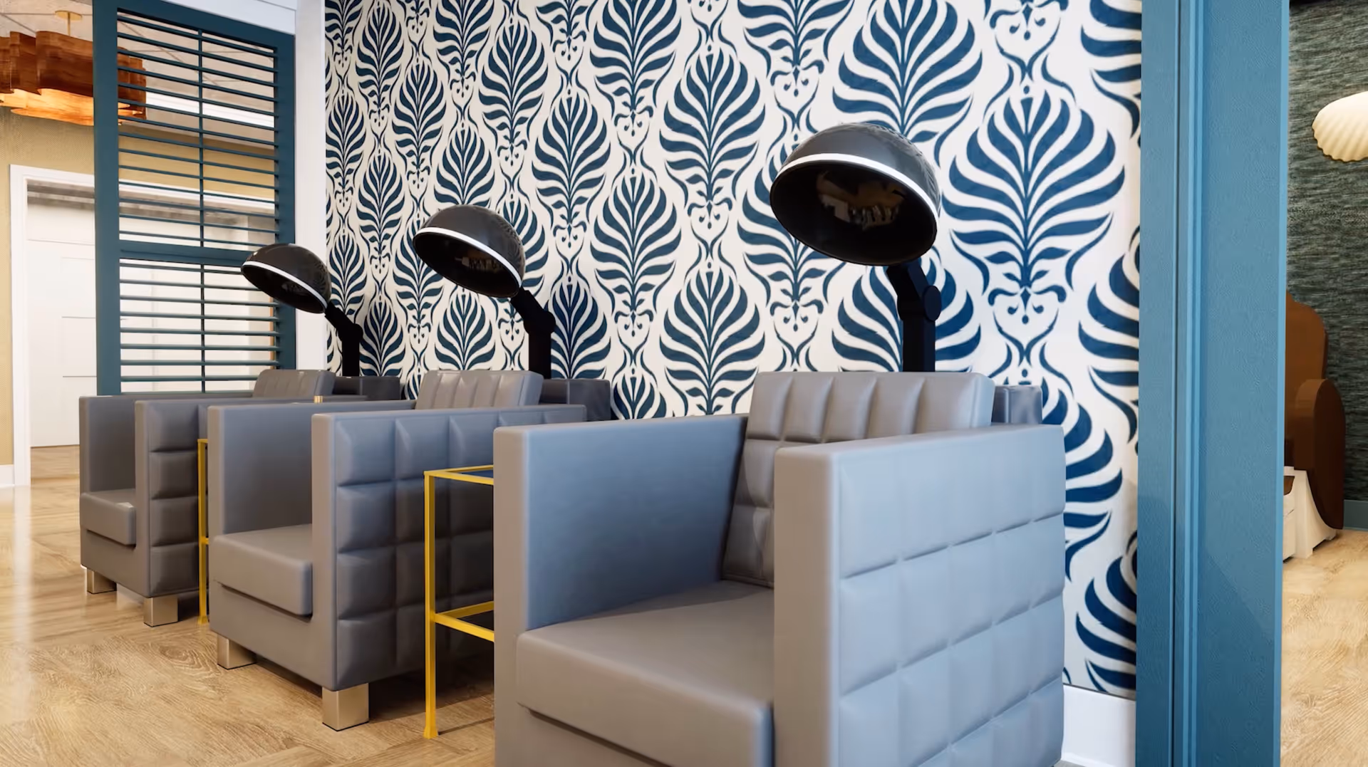 Interior view of a salon area with three gray padded chairs equipped with black hair dryers. The wall behind the chairs features a bold blue and white patterned wallpaper. The floor is light wood, and there is a blue partition with horizontal slats on the left side.