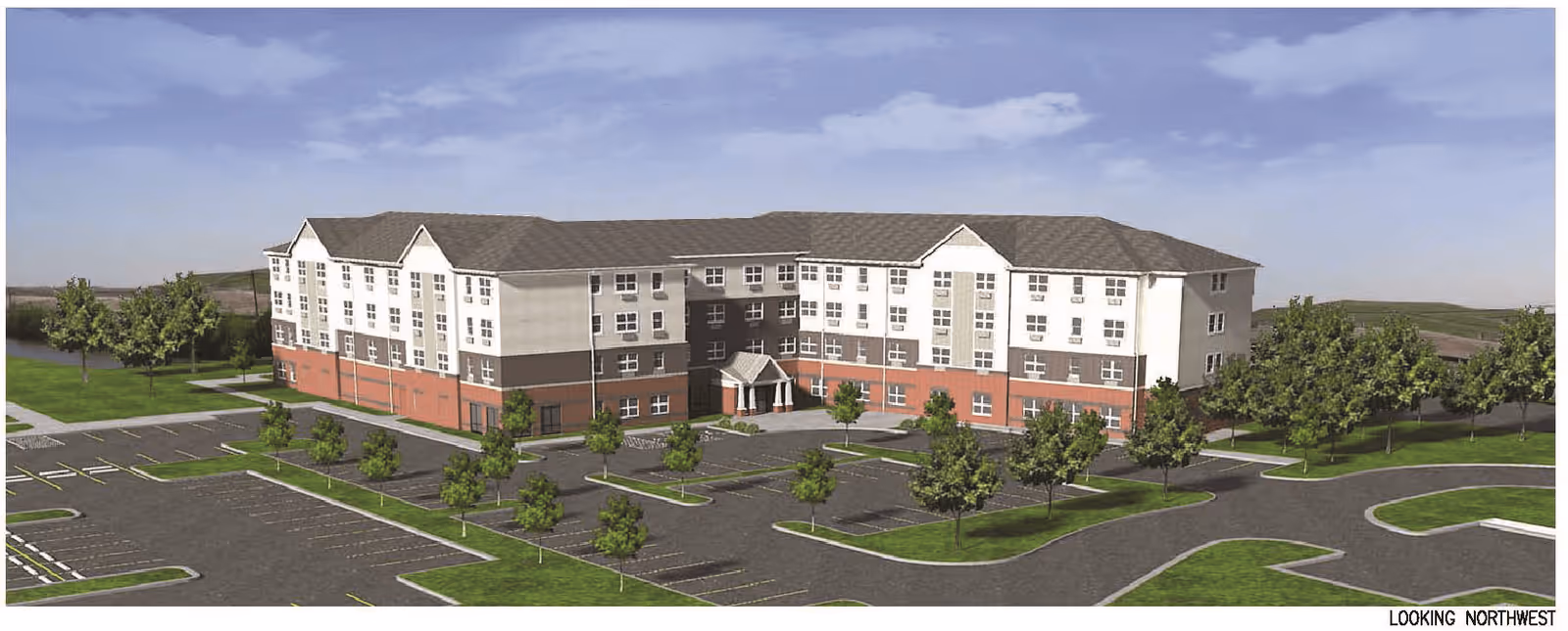 Exterior view of a large, multi-story senior living facility building with a combination of white and red brick facade, surrounded by parking lots and landscaped areas with trees under a partly cloudy sky.
