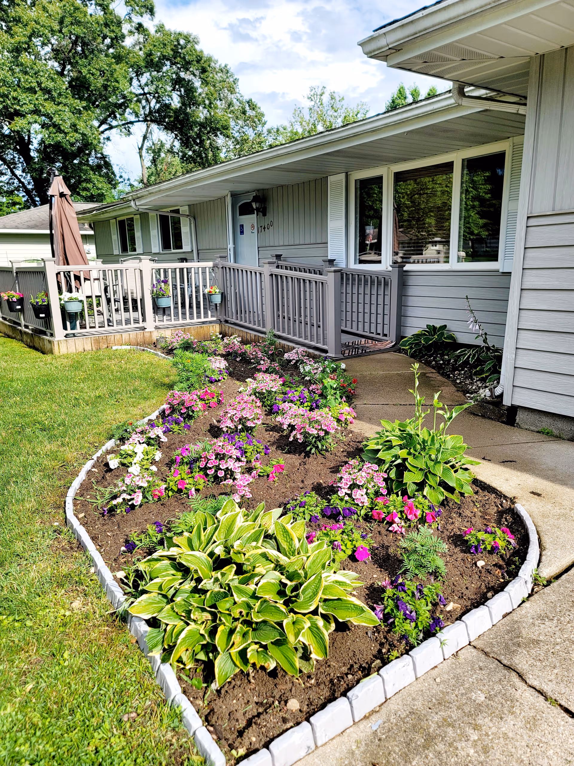 Front exterior of a single-story home with a raised porch and colorful flowerbeds along the walkway.