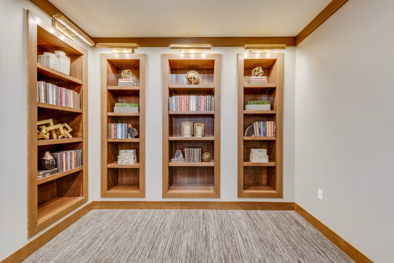 A room with built-in wooden bookshelves filled with books and decorative items, beige walls, and a carpeted floor.