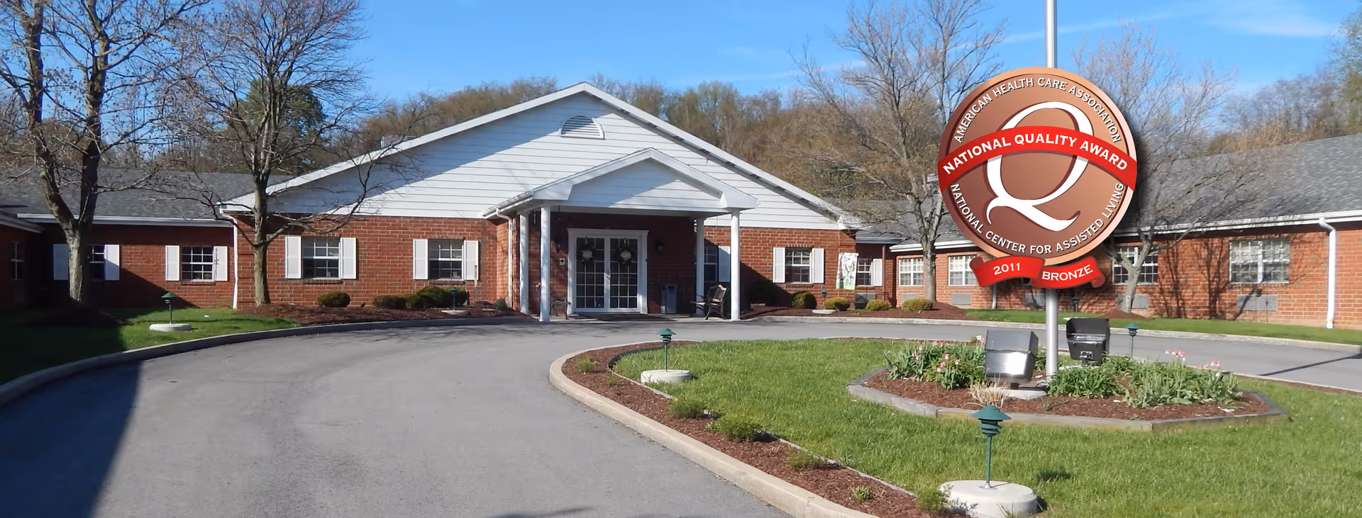Exterior front entrance of a single-story red-brick senior living building with a covered portico and circular driveway.