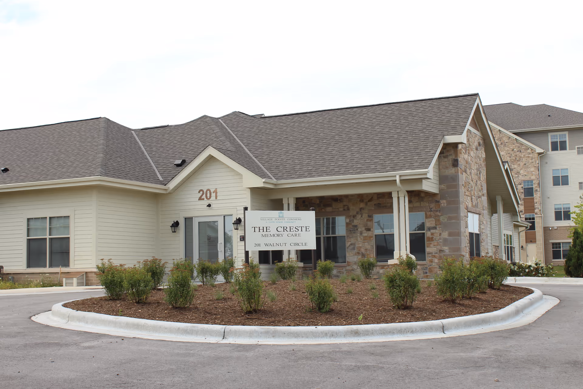 Front of a single-story memory care building with a sign reading "The Creste Memory Care" and a landscaped circular driveway.