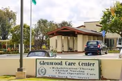 Front entrance of Glenwood Care Center showing the building, driveway with parked cars, and a sign in the foreground.