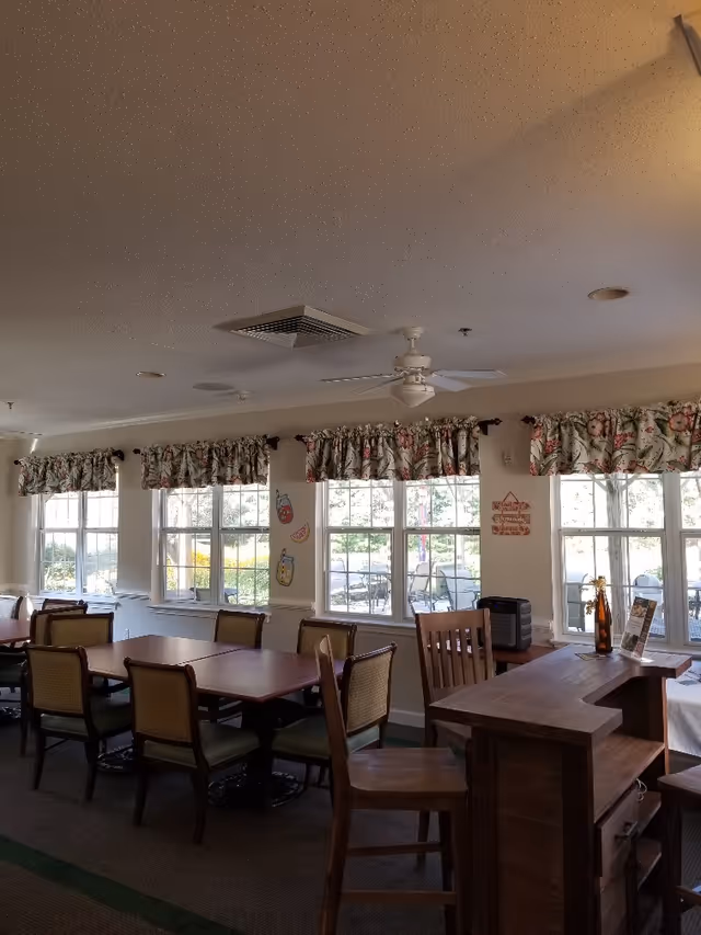 Dining room with multiple tables and chairs, windows with floral valances, and a ceiling fan.