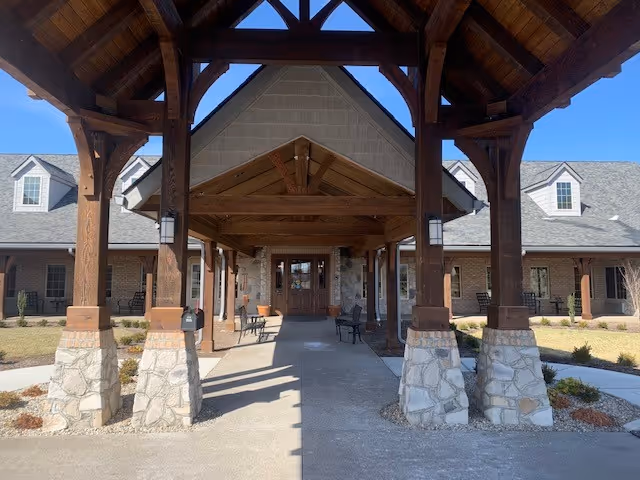 Covered wooden porte-cochère with stone columns leading to the front entrance of a brick building.
