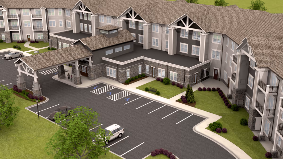 Aerial view of the entrance and parking area of a senior living facility named Monark Grove Madison, showing a large multi-story building with a covered drop-off area, several parked cars, landscaped greenery, and accessible parking spaces.