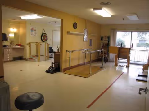 Interior rehabilitation room with parallel bars, therapy equipment, and a doorway to outside.
