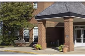 Front entrance of Bayview Health Care showing a covered brick porte-cochère with columns, potted plants, and a bench.
