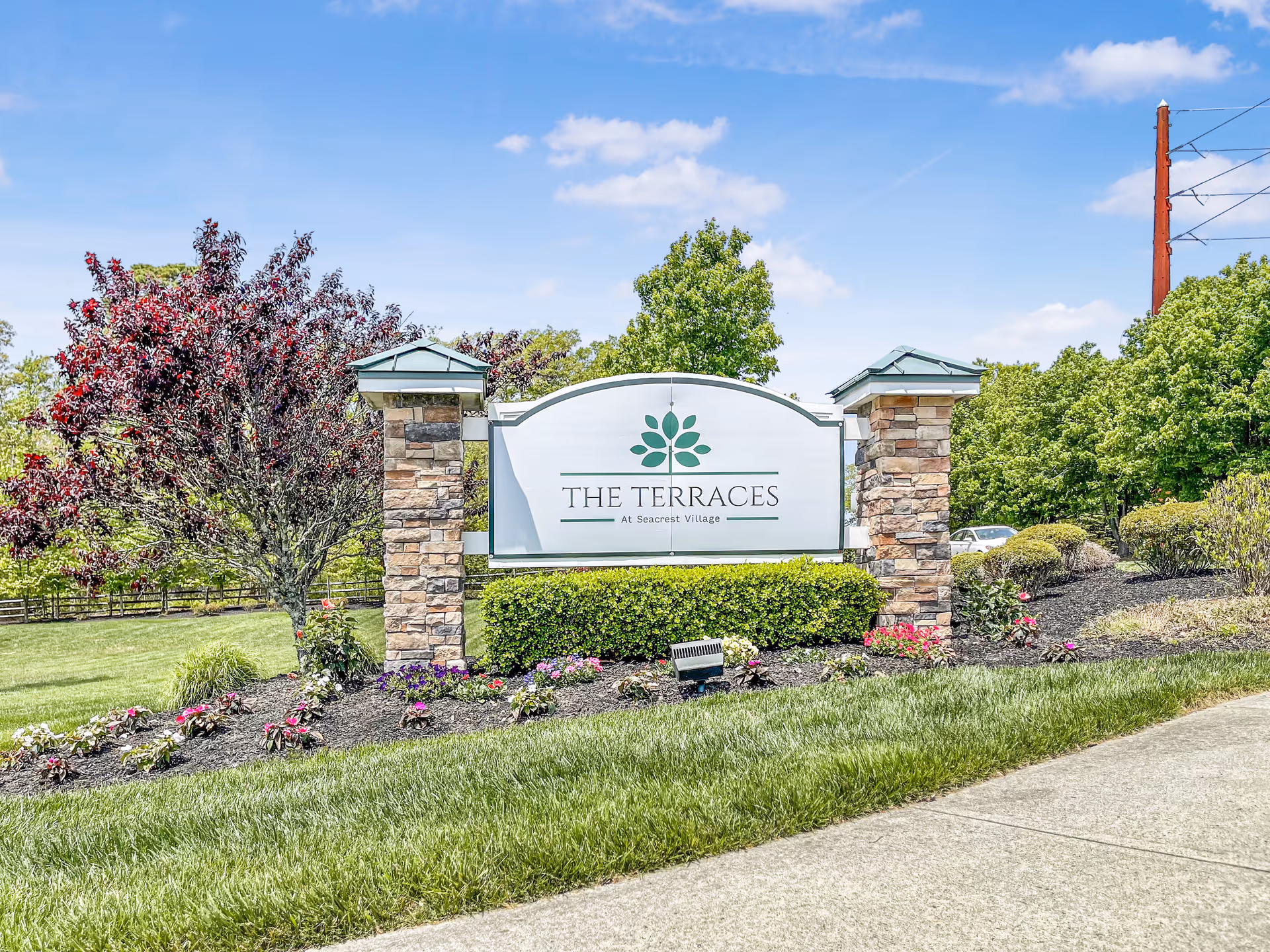 Entrance sign reading "The Terraces at Seacrest Village" surrounded by landscaped flower beds and trees