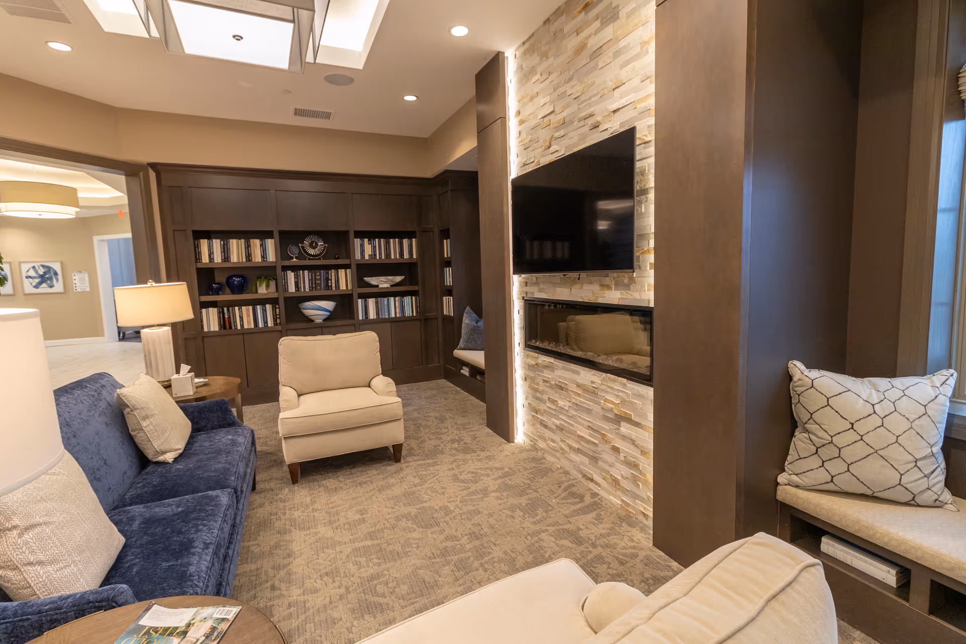 Cozy common living room with sofas and armchairs, a built-in bookshelf, and a wall-mounted TV above a fireplace.