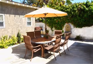 Outdoor patio set with round table, six chairs, and umbrella in sunny courtyard.